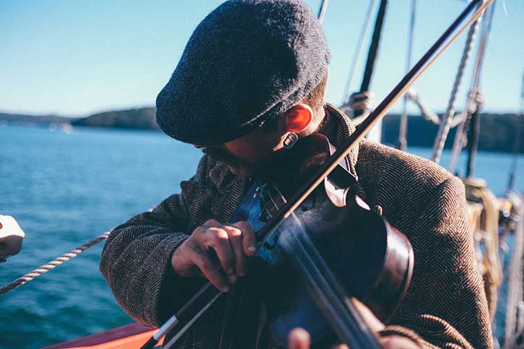 A man with a flat cap is playing a fiddle on the Galway Girl Cruises boat. Galway Girl Cruises operates daily Galway Bay tours.